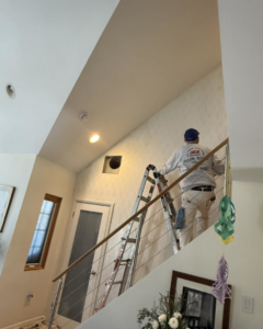 A person on a ladder painting a high interior wall, a service offered by Spinosa Construction And Maintenance in Tewksbury, MA.