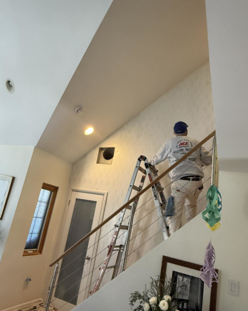 A person on a ladder painting a high interior wall, a service offered by Spinosa Construction And Maintenance in Tewksbury, MA.