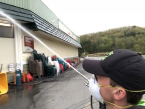 A person in a mask performing pressure washing on a building exterior for Infinity Maintenance Services, Inc. in Brattleboro, VT.