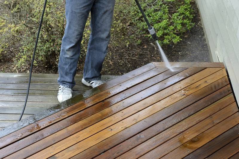 A person pressure washing a wooden deck, a common handyman service offered by Gerald Jones Company in Durham, NC.
