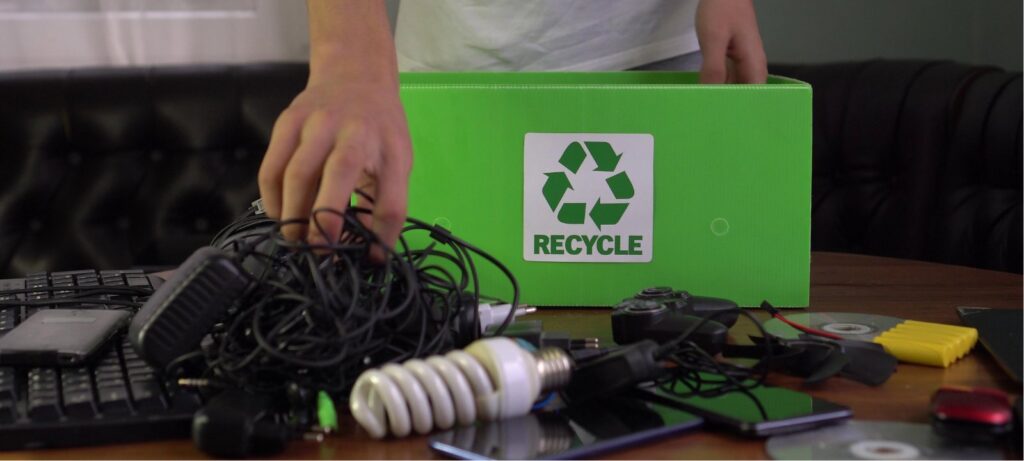 A person placing various e-waste items into a green recycle box for E-Waste Recovery Systems in Sacramento, CA.