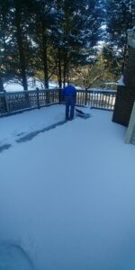 A person actively shoveling snow off a wooden deck, a snow removal service by C&C LAWN CARE,MOVING & TRASH REMOVAL in Baltimore, MD