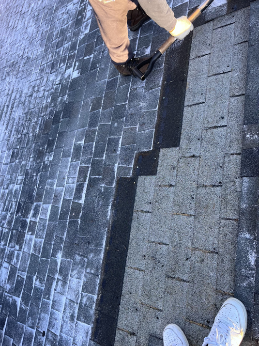 A person actively shoveling snow off an asphalt shingle roof, demonstrating snow removal services by Crown Remodeling in Owings Mills, MD.
