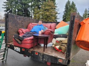 A worker sitting on an armchair in a truck loaded with various junk items for Glenn's Junk & Landscape Hauling in Renton, WA.