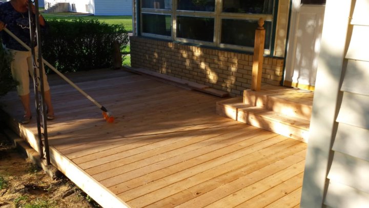 A person sweeping a newly installed wooden deck, showcasing a project by The Creative Carpenter in Minot, ND.