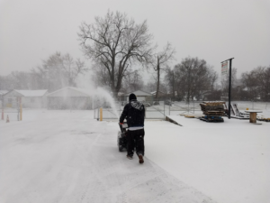 A person operating a snow blower to clear a path during a snowfall, a service provided by 24/7 Snow Removal & Salting in Indianapolis, IN.
