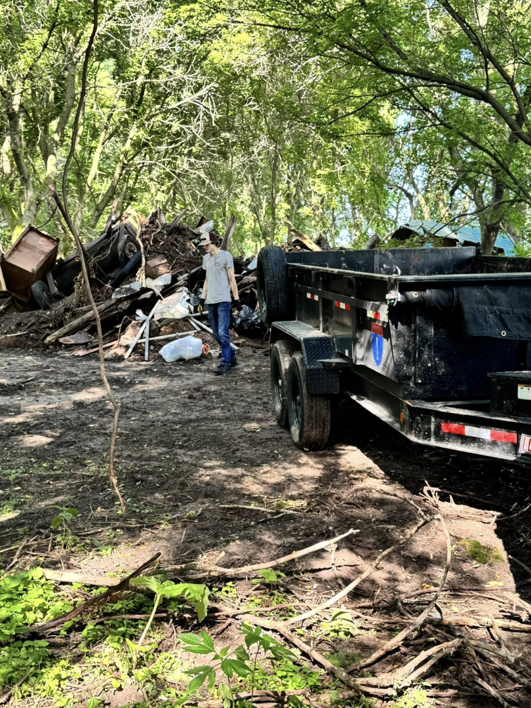 A person standing next to a large pile of junk and a dump trailer, ready for removal by Speedy Scrap Junk Removal LLC in Portage, WI.