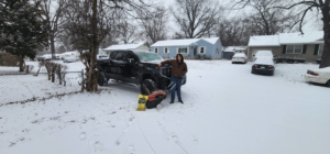 A person standing with a snow spreader and pickup truck, ready for snow removal services by Brother's Keeper Construction in Spokane, WA