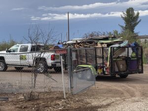 A white pickup truck with a trailer full of various junk and debris, ready for removal by Roadrunner JunkSmart Solutions LLC in Las Cruces, NM.