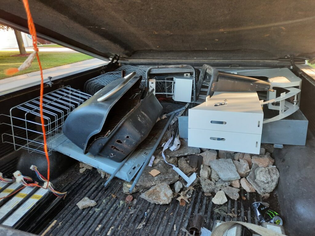 The bed of a pickup truck filled with various junk items including a grill, metal racks, and rocks, handled by Sunshine junk removal LLC in Lake City, MN.