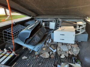 The bed of a pickup truck filled with various junk items including a grill, metal racks, and rocks, handled by Sunshine junk removal LLC in Lake City, MN.