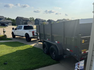 A white pickup truck with a large dump trailer parked in a residential driveway for junk removal by MusGo Junk Co in O'Fallon, MO.