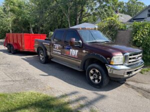 A The Dump Town pickup truck towing a red dump trailer, ready for junk removal services in Detroit, MI.