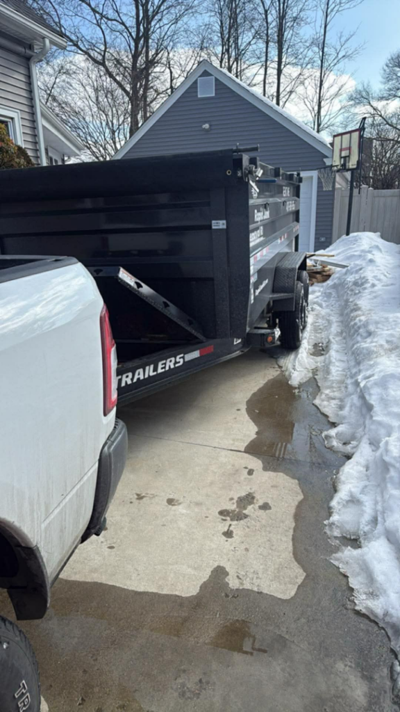 A pickup truck with a dumpster trailer from Dumpsters RI.com - Dumpster Rentals RI on a residential driveway in Rhode Island.
