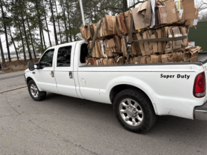 A white pickup truck hauling a large stack of baled cardboard for E&k logistics an Recycling LLC in Hoover, AL.