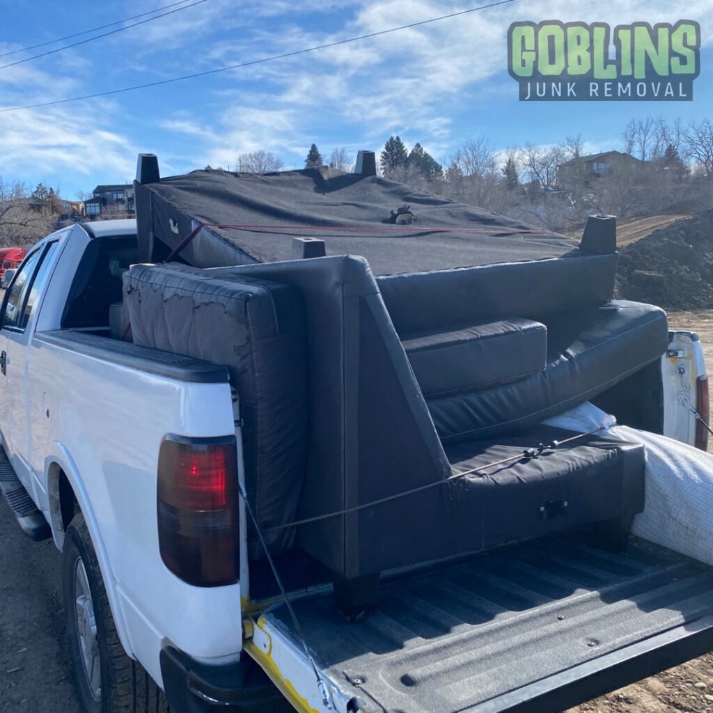 A white pickup truck hauling a large black sofa in its bed, demonstrating junk removal services by Goblins Junk Removal in Wheat Ridge, CO.