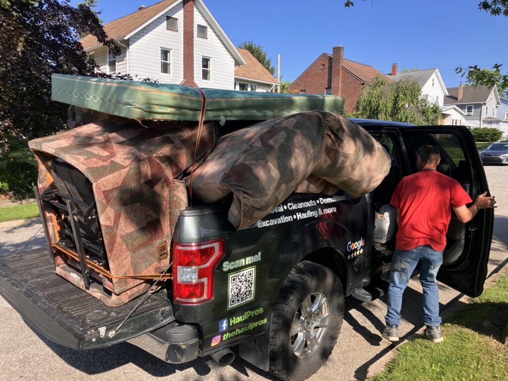A HaulPros pickup truck loaded with large furniture items like a mattress and couch, ready for junk removal in Erie, PA.