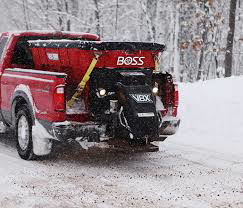 A pickup truck with a salt spreader on a snowy road, equipment available from Handyman Rental in Portland, ME.