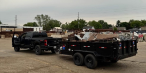 A black pickup truck towing a dump trailer filled with scrap metal and debris, representing transportation services by Speedy Scrap Junk Removal LLC in Portage, WI.
