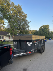 A pickup truck towing a dump trailer with wooden extensions on a residential street for Salt Creek Disposal in Bowling Green, KY.