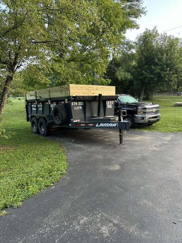 A pickup truck towing an empty dump trailer with wooden extensions on a residential driveway from Salt Creek Disposal in Bowling Green, KY.