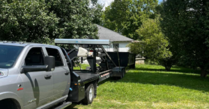 A grey pickup truck with a flatbed trailer carrying a roll-off dumpster for O'Lakes Dumpster Rental in Lexington, KY.