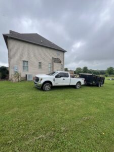 A white pickup truck towing a utility trailer, used for junk removal by Dumpin' Junk in Martinsburg, WV.