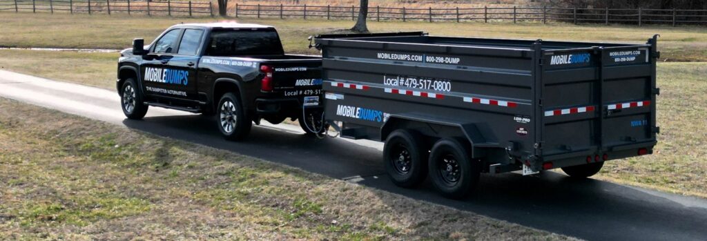 A pickup truck transporting a Mobiledumps trailer on a road for junk removal services in Rogers, AR.