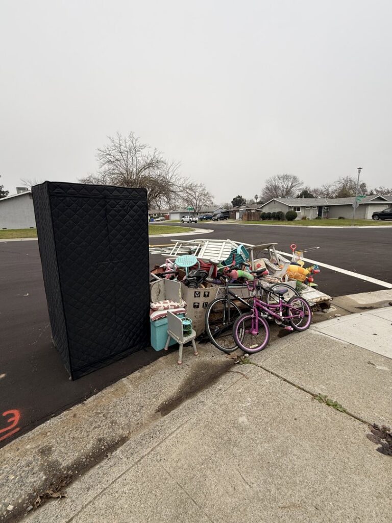 A pile of household items, including a large black cabinet and bicycles, placed on the curb for junk removal by Junk Away & Cleaning in Sacramento, CA.