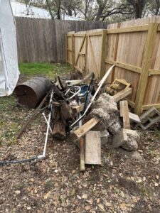 A large pile of mixed debris, including wood, metal, and concrete blocks, in a yard for cleanout by SATX Junk-A-Haulics in San Antonio, TX.