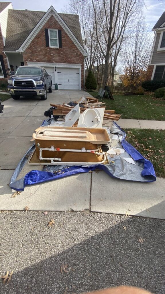 A pile of old bathroom fixtures and construction debris on a tarp in a driveway, ready for junk removal by Haul-Away in Overland Park, KS.