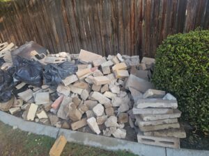 A large pile of bricks and concrete debris awaiting removal next to a wooden fence by Bakersfield Roll-Off Service in Bakersfield, CA.