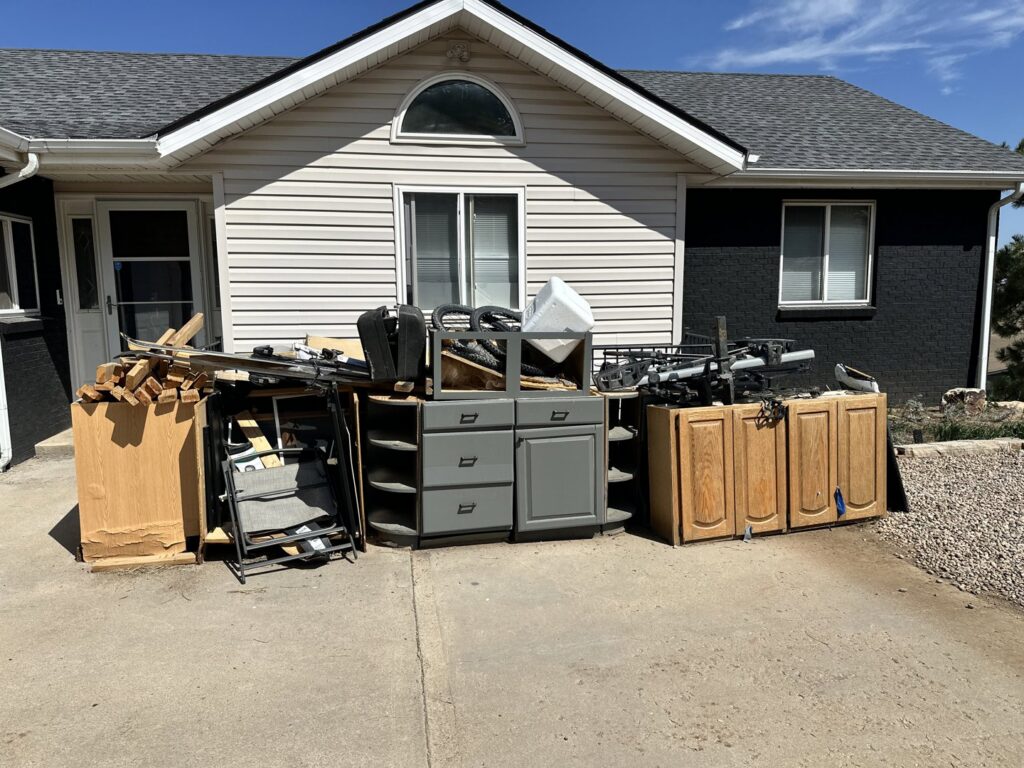 A large pile of old cabinets, wood, and construction debris outside a house, ready for removal by Hagen's Junk Removal in Fort Collins, CO.