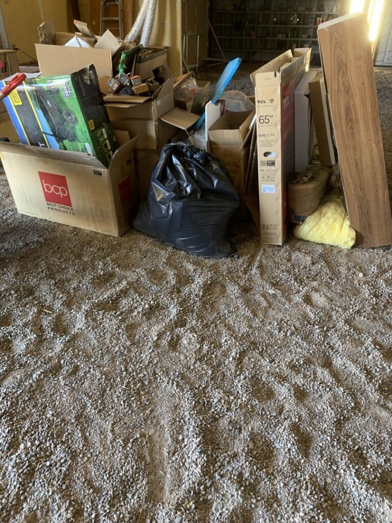 A pile of cardboard boxes, a black trash bag, and other debris on a gravel floor, ready for removal by Roadrunner JunkSmart Solutions LLC in Las Cruces, NM.