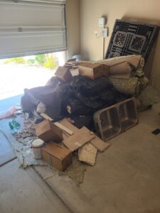 A pile of rolled-up carpets, black trash bags, cardboard boxes, and old sinks in a garage for Road Dogz Hauling in Las Vegas, NV.
