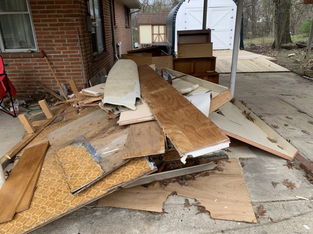 A pile of wood, old flooring, and construction debris outside a house, ready for removal by You Call We Haul Junk Removal in Milwaukee, WI.