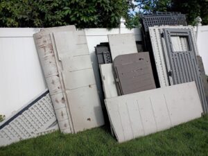 A pile of disassembled plastic shed panels and parts in a grassy area, indicating a junk removal service by Junk-O-Haulics in Westmoreland, TN.