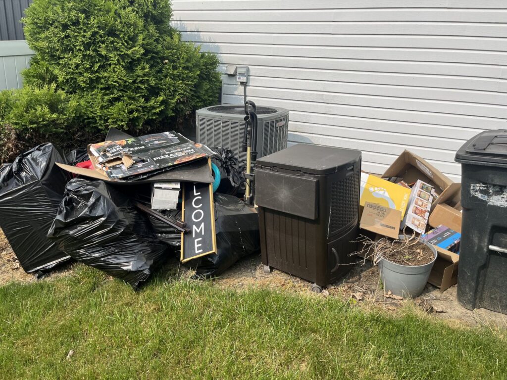 A pile of household junk, including black trash bags, cardboard boxes, and an old AC unit, ready for removal by You Call We Haul Junk Removal in Milwaukee, WI.