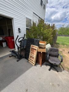 A pile of household junk including an elliptical, table, and chair outside a garage, ready for removal by Dumpin' Junk in Martinsburg, WV.