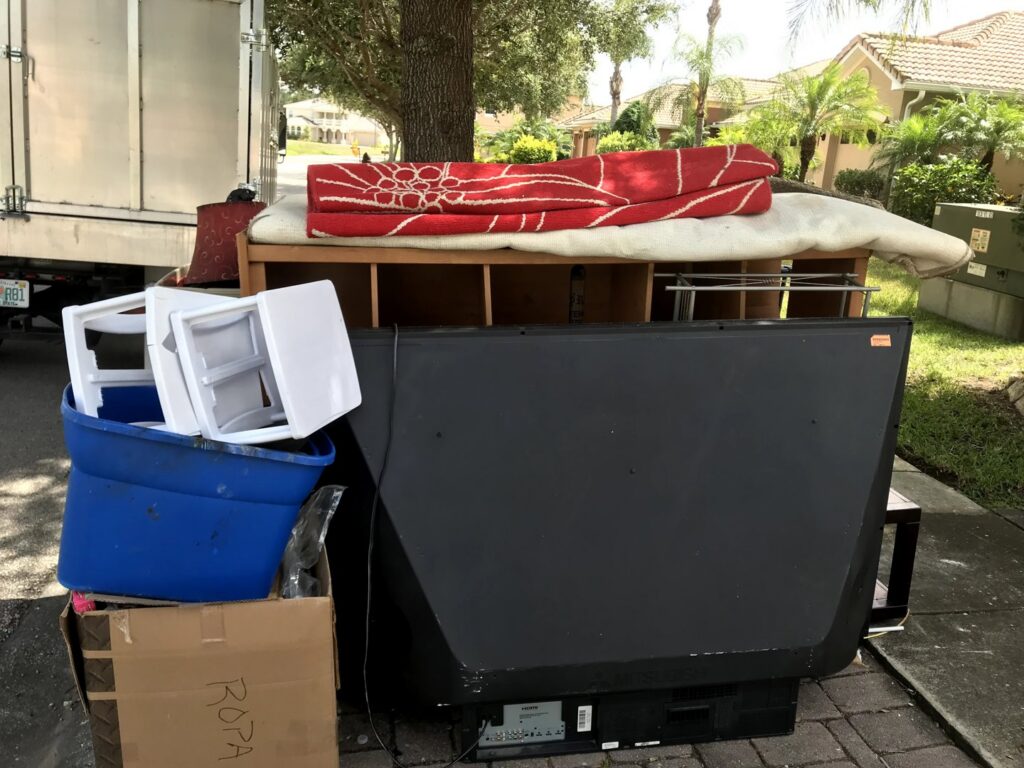 A pile of household junk including a TV, furniture, and boxes on the curb, ready for removal by Pro Dumpsters & Junk Removal in Orlando, FL.