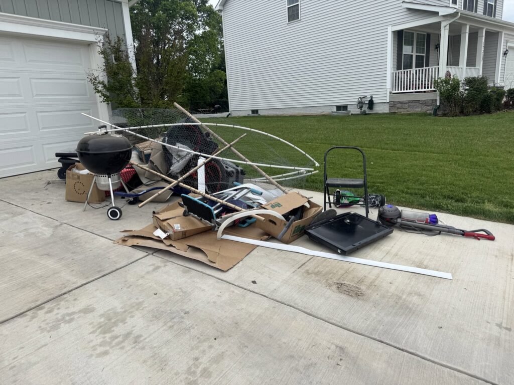 A pile of household junk including a grill, boxes, and broken items on a driveway for Quick Lift Junk Removal in Hagerstown, MD.