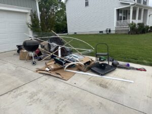 A pile of household junk including a grill, boxes, and broken items on a driveway for Quick Lift Junk Removal in Hagerstown, MD.