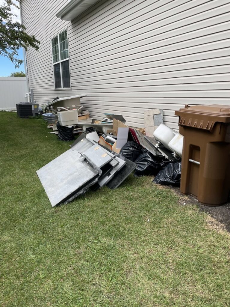 A large pile of household junk and debris awaiting removal next to a residential home by Anywhere Dumpster Rental in Bolingbrook Area, IL.