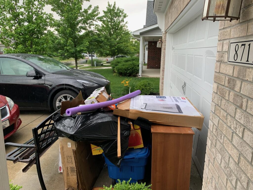 A pile of household junk and trash bags next to a driveway, ready for removal by Indy Trash Guy in Fishers, IN.