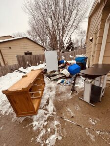 A large pile of household junk, old furniture, and debris in a snowy backyard, awaiting removal by WeHaul Hauling & Junk Removal in Sioux Falls, SD.