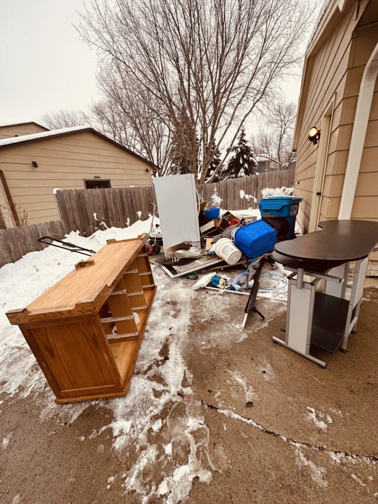 A large pile of household junk, old furniture, and debris in a snowy backyard, awaiting removal by WeHaul Hauling & Junk Removal in Sioux Falls, SD.