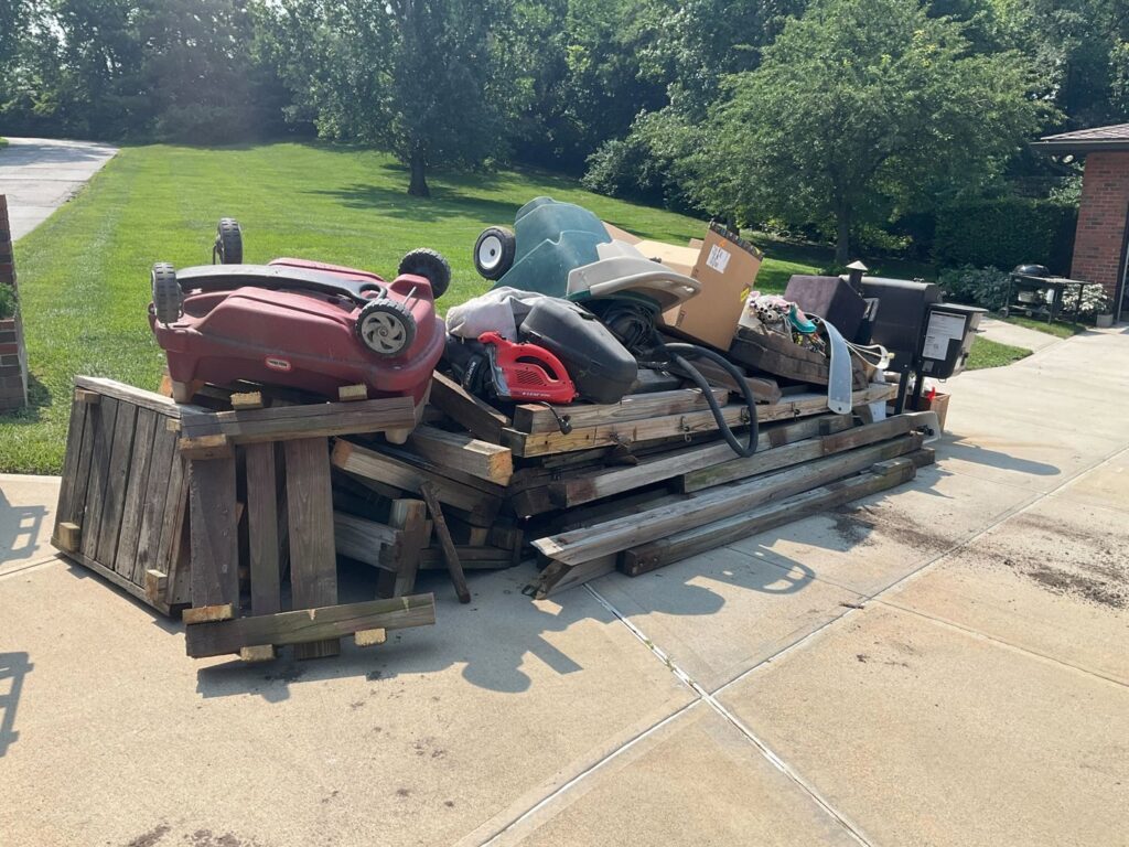 A large pile of wooden pallets, a lawnmower, and other junk in a driveway, ready for pickup by Midwest Removal in Omaha, NE.