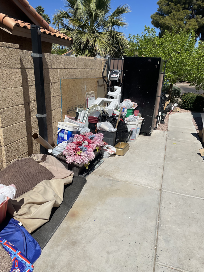 A large pile of household junk and debris next to a dumpster, ready for removal by M&O Dumpster Services in Tolleson, AZ.