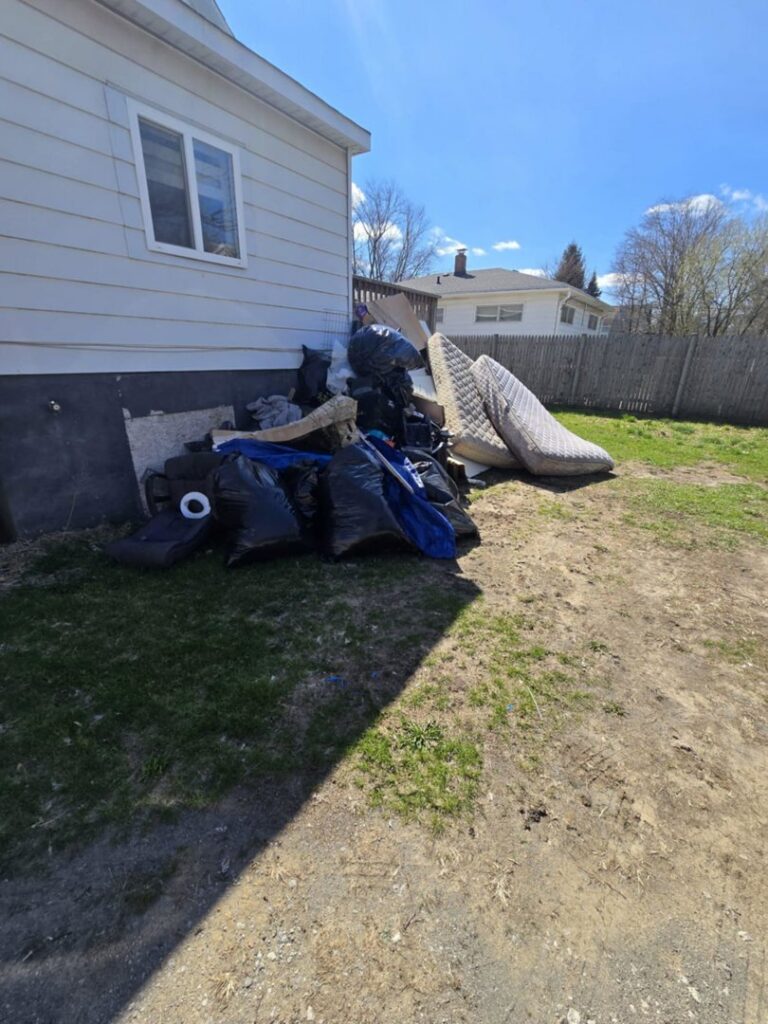 A pile of mattresses, bags, and debris stacked next to the side of a house, awaiting junk removal by Merica JunkBoss LLC in Hammond, IN.
