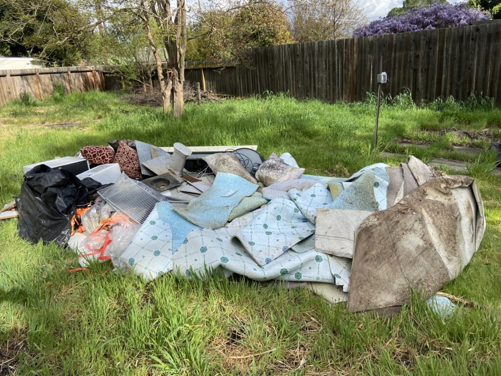 A large pile of old carpet and construction debris in a grassy area, ready for removal by Sac Junk in Rancho Cordova, CA